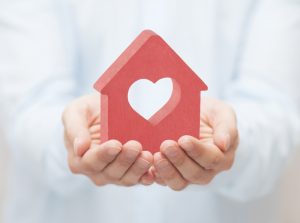 two-hands-holding-a-red-house-shaped-block-with-a-heart-cutout